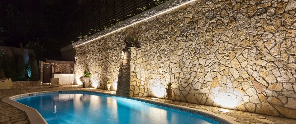 Wall-washing landscape lighting technique used in Phoenix, AZ, on a stone wall by a pool.